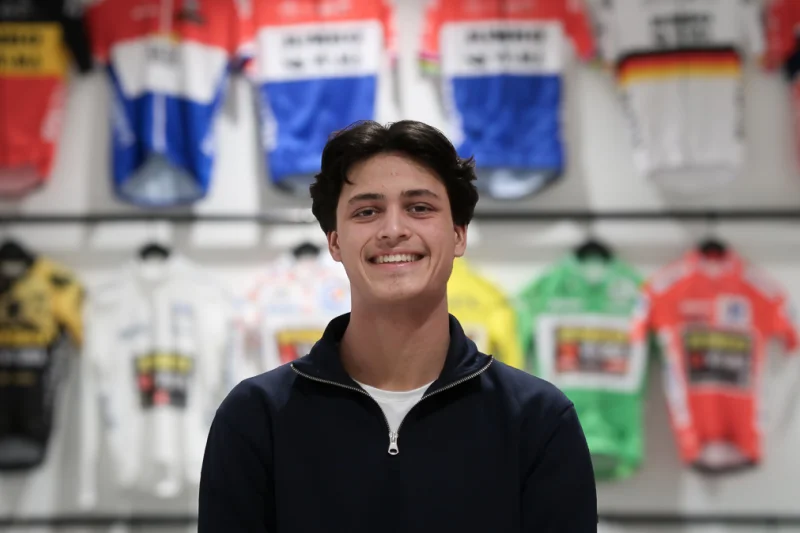 Tygho volgt de opleiding Medewerker sportmarketing en poseert voor een muur met sportshirts. Deze foto is genomen op zijn stageadres.