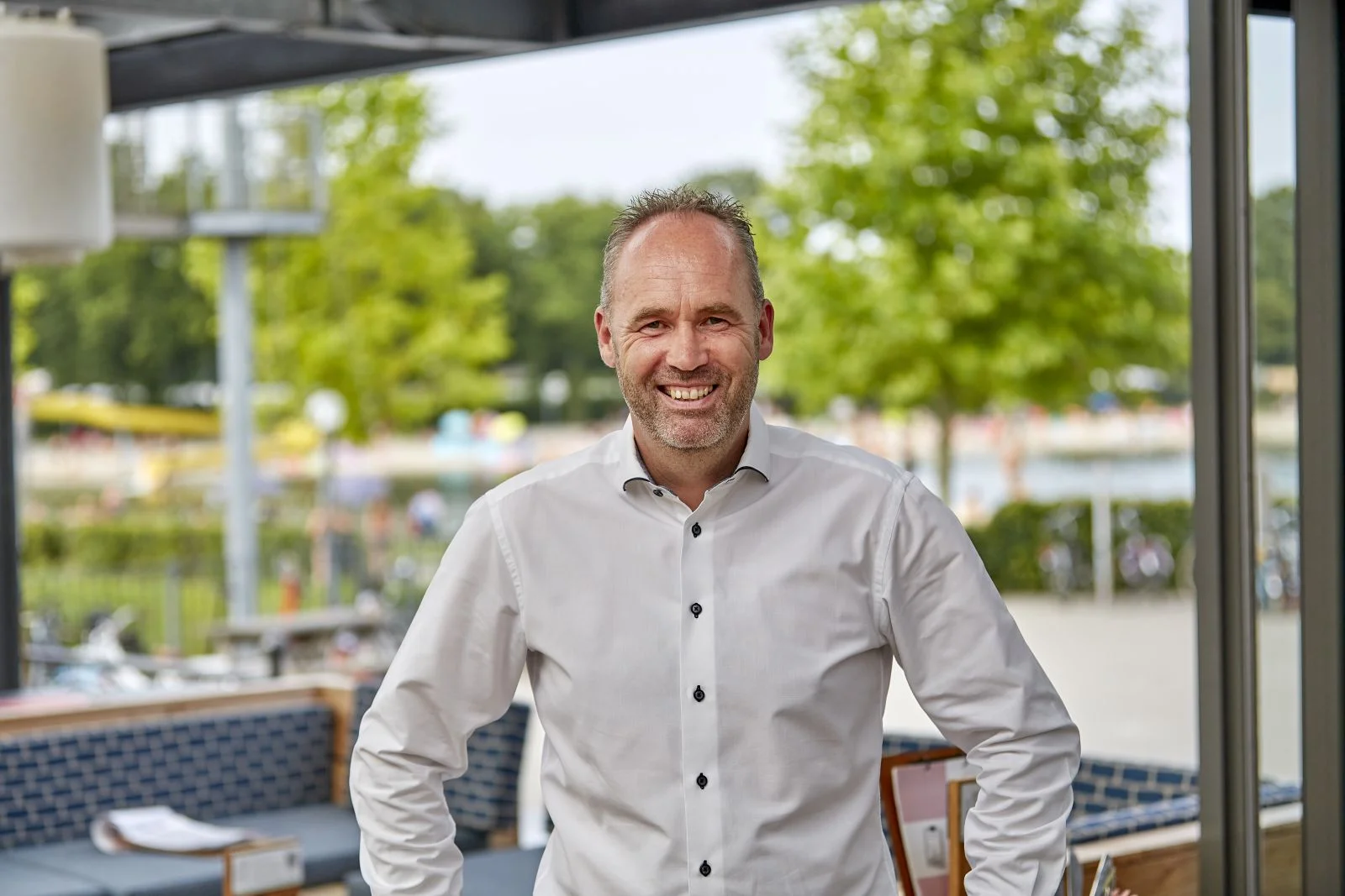 Michel Huigevoort, directeur TerSpegelt en oud-student De Rooi Pannen, lacht richting de camera. Recreatiepark TerSpegelt is vaag te zien op de achtergrond.