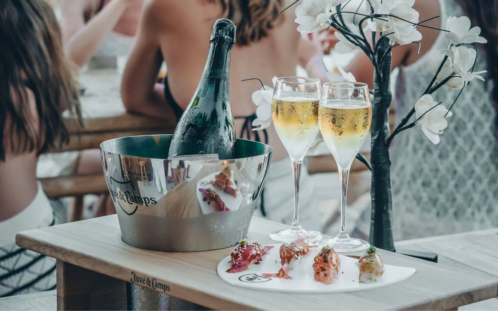 Twee gevulde champagne glazen met daarachter een champagne fles en vier stukjes verse sushi