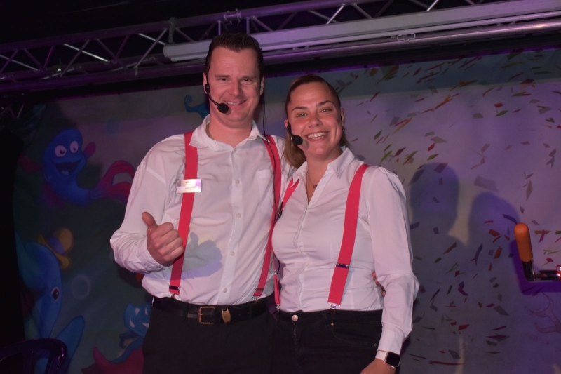 Jordy poseert tijdens zijn werk, in een witte blouse en met microfoon headset, met een collega.