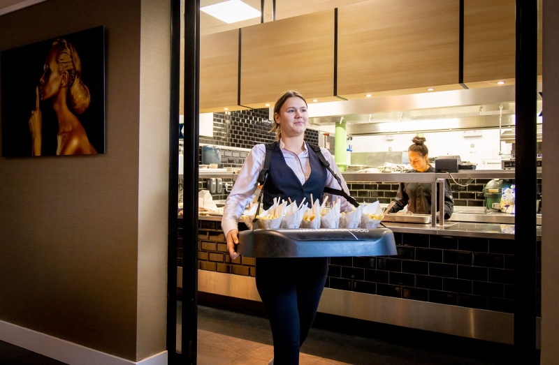 Student van De Rooi Pannen als gastvrouw bij Hotel Nassau. Ze pakt een gerecht aan uit de keuken.