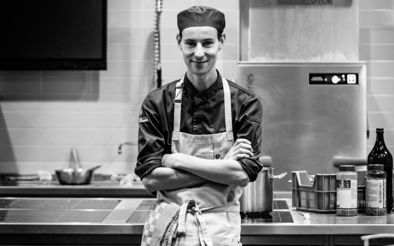 Zwart-witte foto van Beer in de keuken van De Rooi Pannen Tilburg Horeca. Hij heeft kokskleding aan en zijn armen over elkaar.