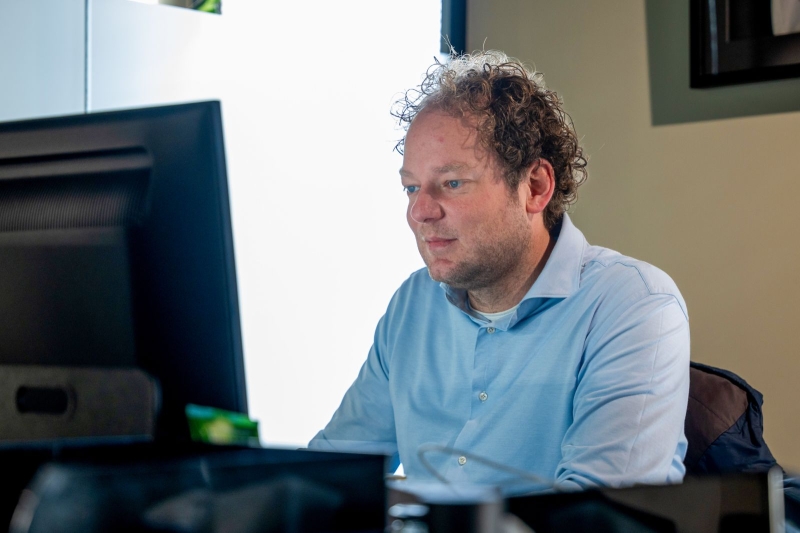 Freek zit achter zijn computer in een lichtblauwe blouse aan.