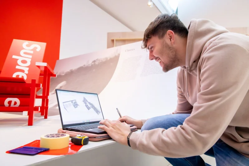 Opleidingen Signmaking bij De Rooi Pannen Tilburg Vormgeving & Signmaking Student Signmaking met zijn laptop in een museum waar hij de signing voor verzorgd.