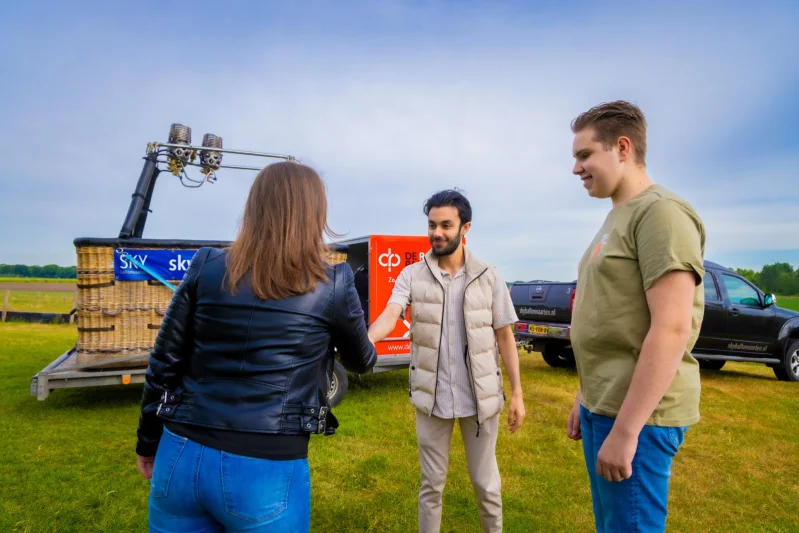 Student van de mbo-opleiding Commercieel medewerker schudt de hand met een klant. Achter hen staat een kar voor een luchtballon.