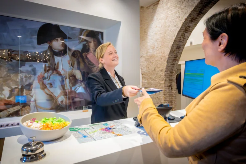 Studenten doen praktijkervaring op tijdens hete mhbo-traject Hotelmanagement. Ze staan een gast te woord bij de receptie van het onderwijshotel in Breda.