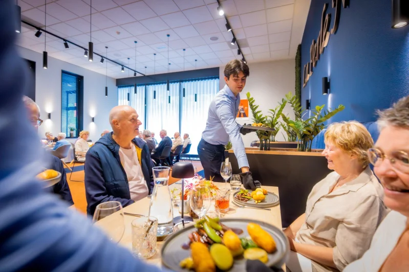 Horeca student serveert een gerecht in een vol restaurant bij De Rooi Pannen Eindhoven.