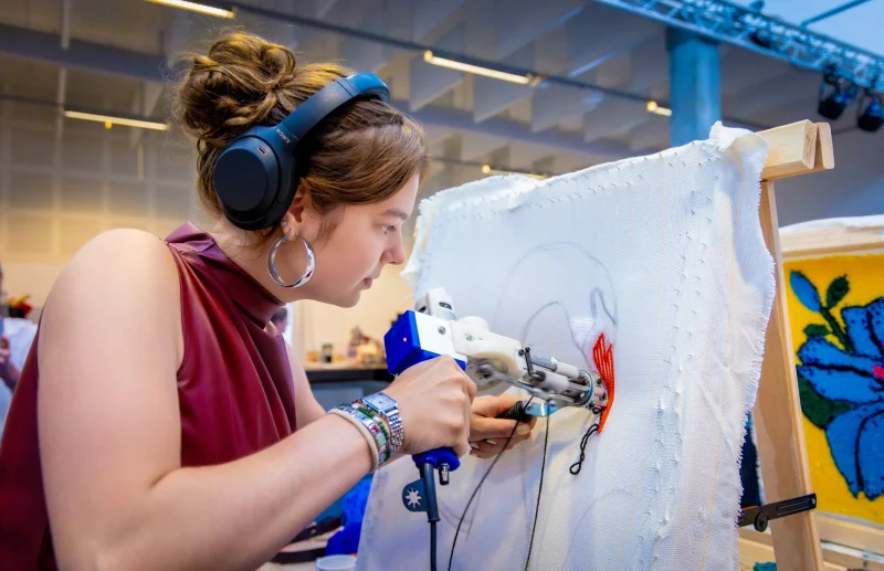 Een student van de mbo-opleiding Ruimtelijk vormgever is aan het tuften op een doek in het atelier.