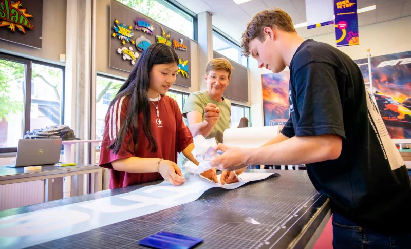 Studenten van de mbo-opleiding Medewerker sign werken samen aan een signing op school. De student helpt hen.