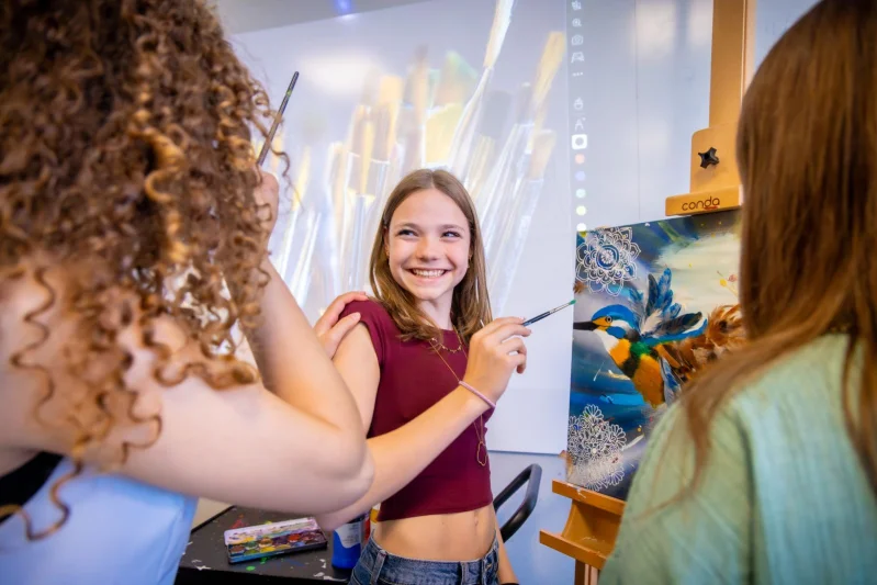 Kader bij het vmbo van De Rooi Pannen Tilburg Drie leerlingen van het vmbo in Tilburg lachen naar elkaar terwijl ze een penseel vasthebben en aan het schilderen zijn.