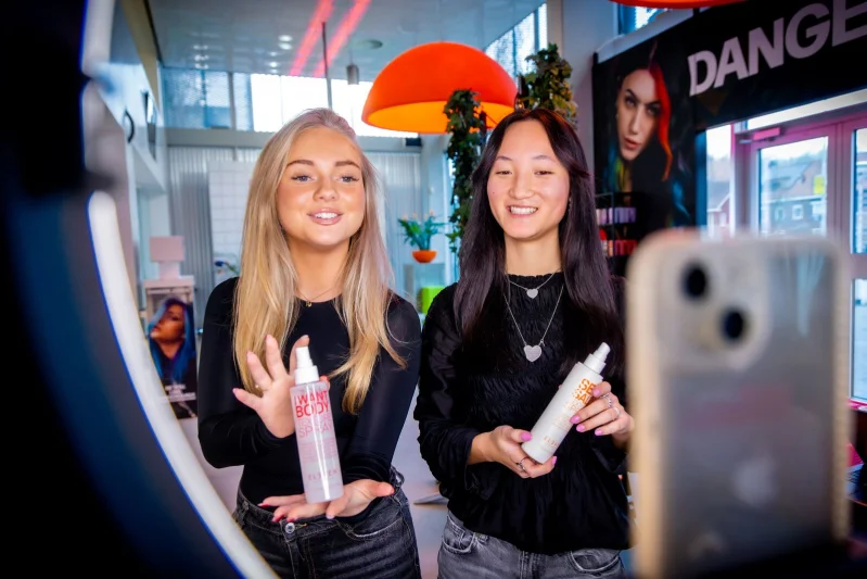 Twee studenten nemen een TikTok-filmpje op met hun telefoon en een ringlamp. Ze laten verzorgingsproducten zien.