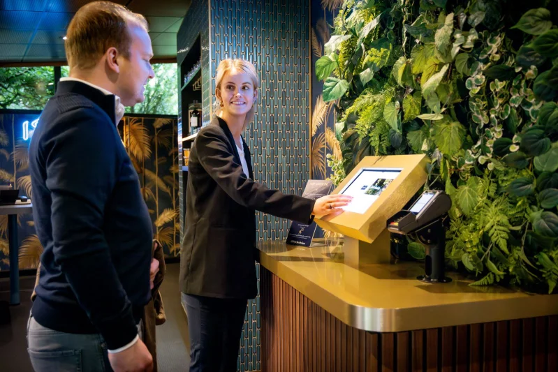Student Medewerker hospitality in gesprek met twee gasten aan tafel in het restaurant van De Rooi Pannen.