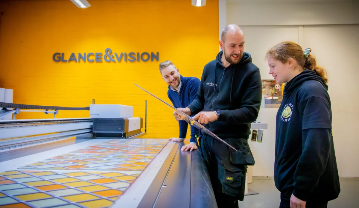 De twee broers leggen iets uit aan een stagiaire in de werkplaats bij signbedrijf Glance & Vision.