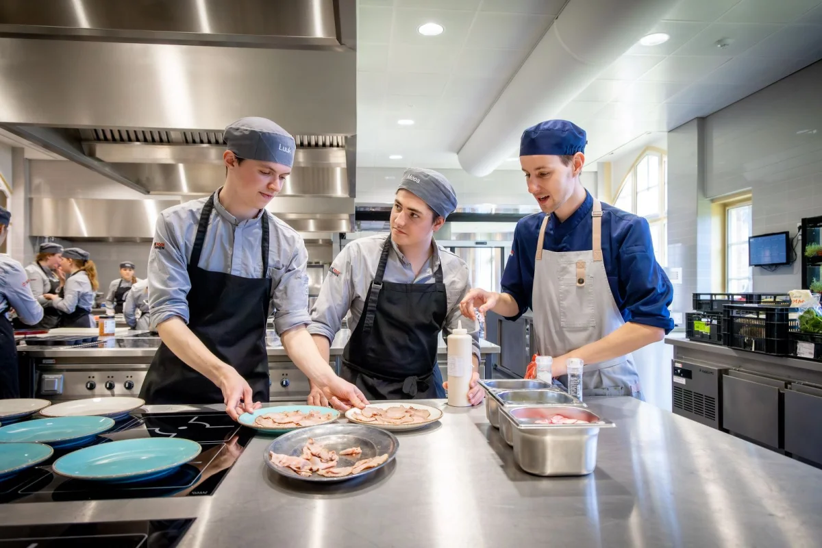 Twee studenten en een docent staan naast elkaar in de keuken van De Rooi Pannen.